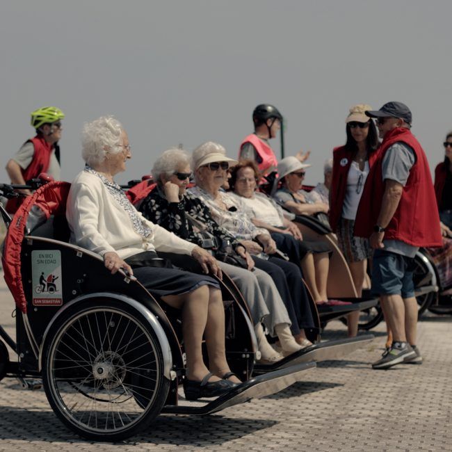 Grupo de personas montadas en los triciclos y los pasajeros al lado, cerca del mar