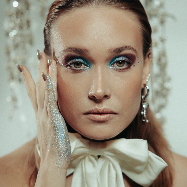 Mujer con maquillaje azul y malva en los ojos, con chaqueta de brillos